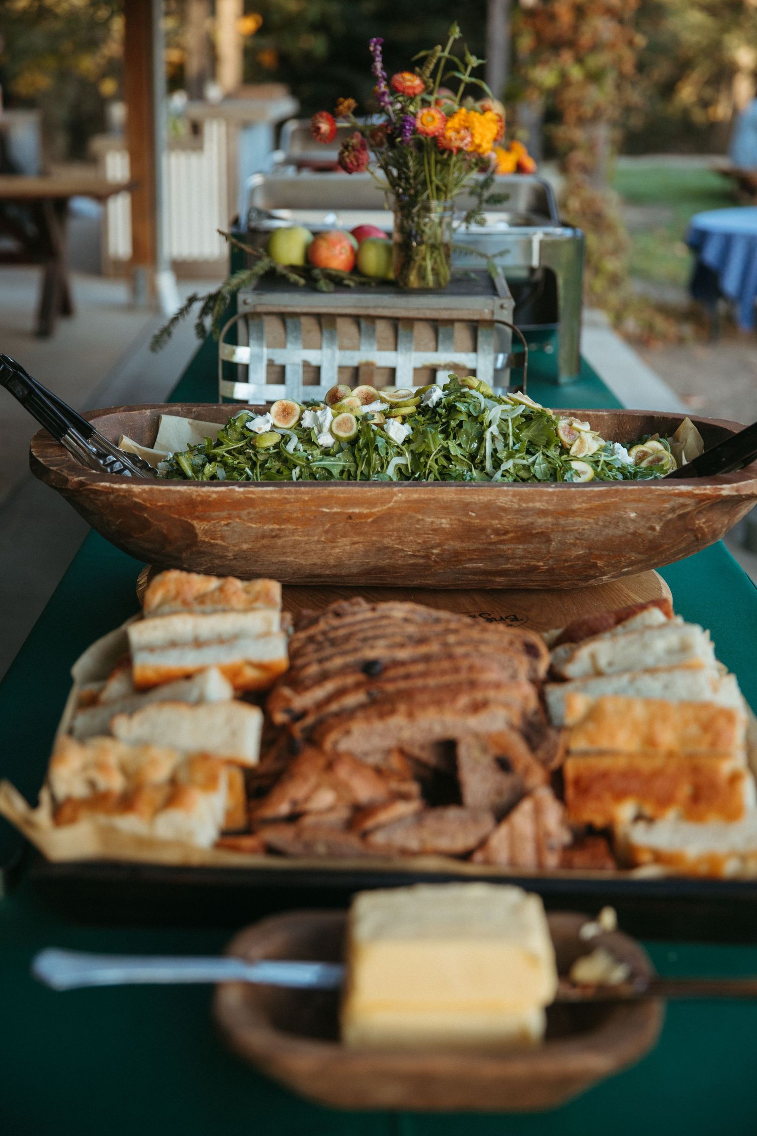 Buffet table with wooden salad bowl and sliced bread platter at outdoor event.