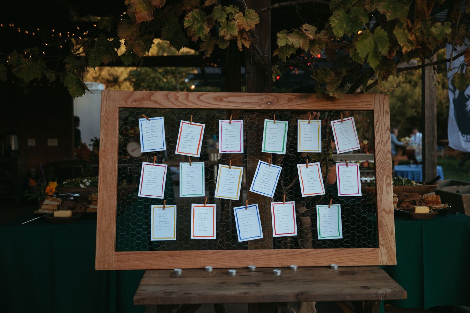 Wedding seating chart displayed on dark green board in wooden frame.