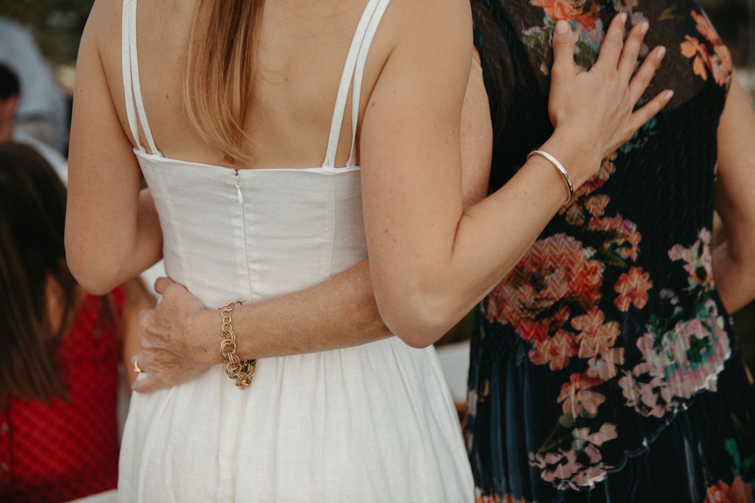 Close-up of white wedding dress buttons and floral dress at outdoor celebration.