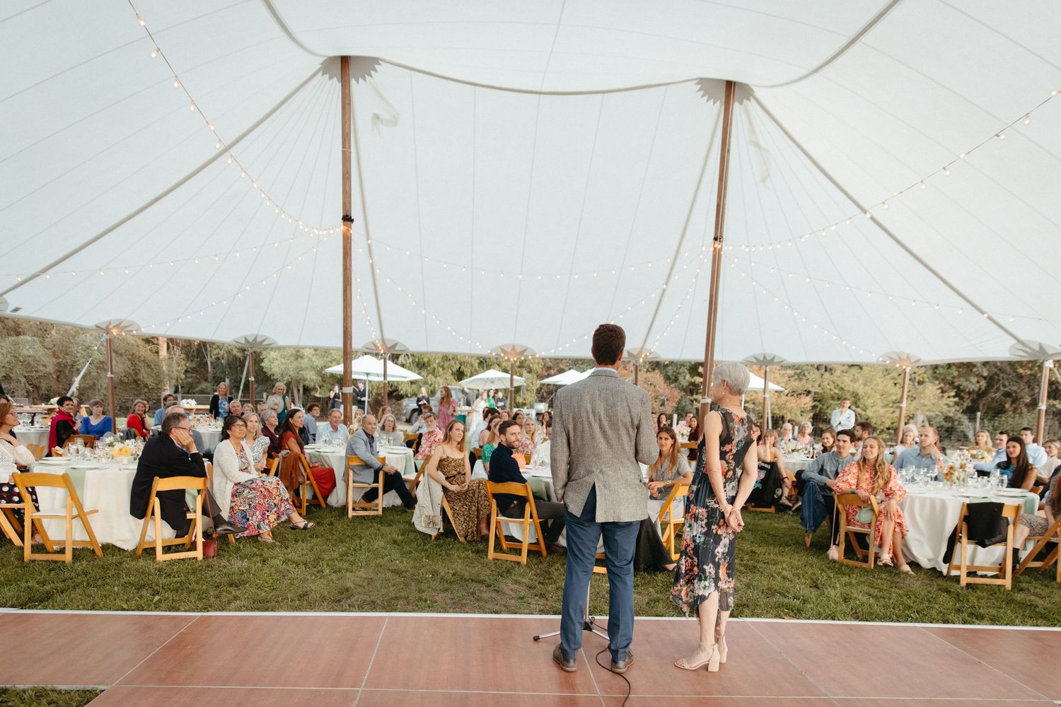 Guests embracing during emotional moment at outdoor celebration under string lights.