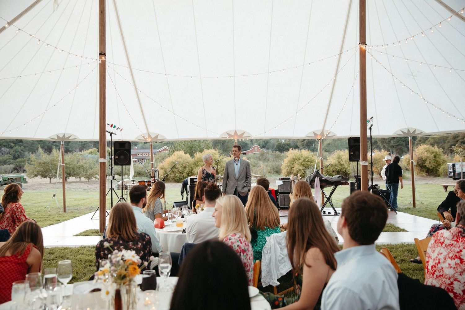 Couple overlooking seated guests from wooden dance floor at outdoor reception.