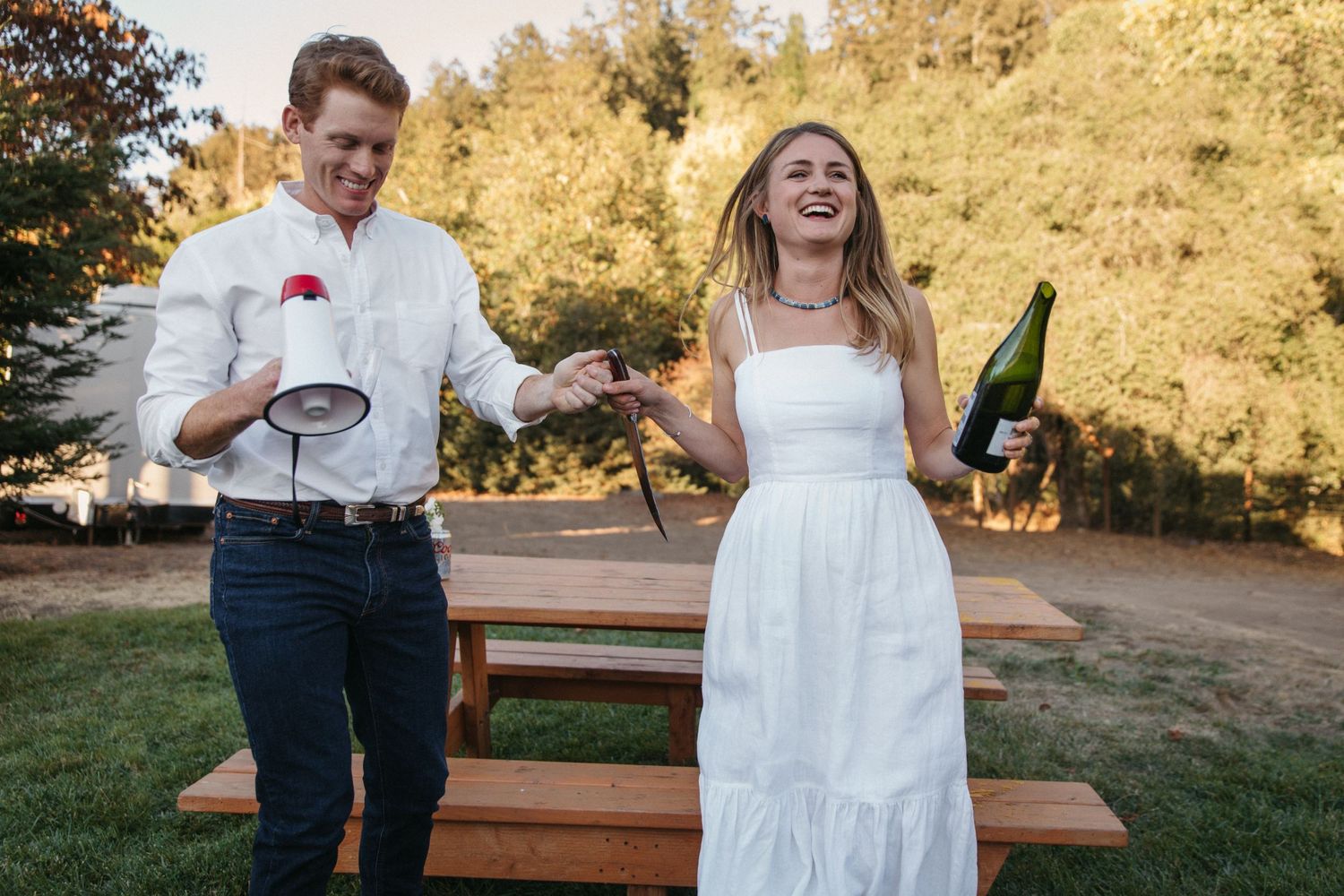 A couple shares a fun moment with megaphones and drinks on a wooden platform outdoors.