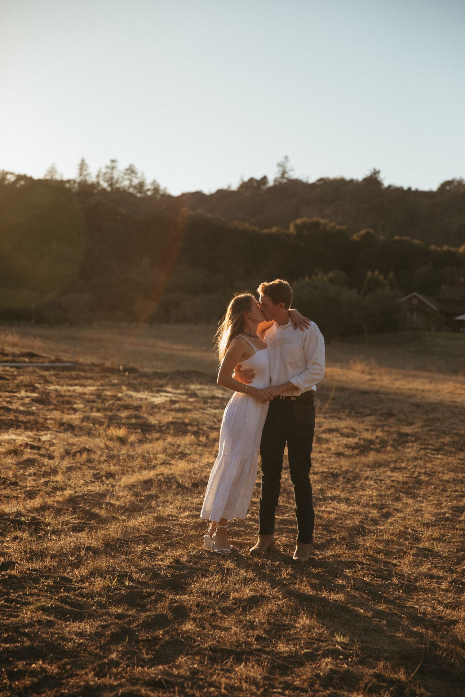 Black and white photo of couple embracing in an open field at sunset.