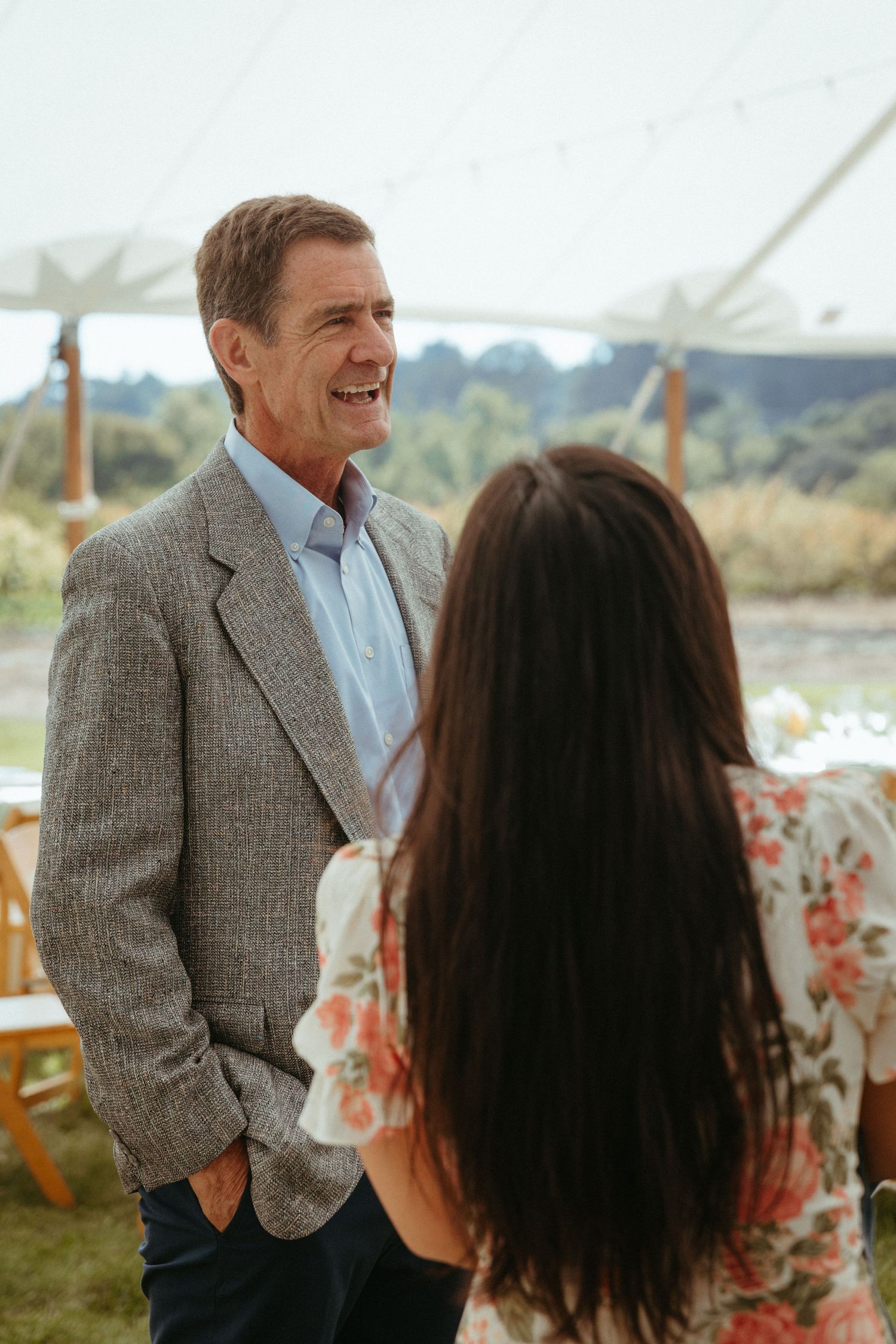 Two people having an animated conversation outdoors under a tent at a social gathering.