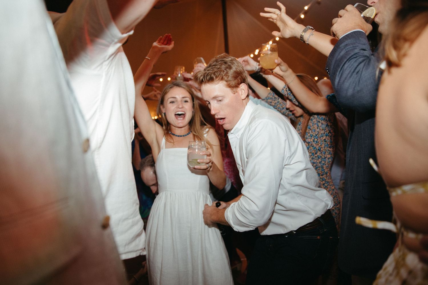 Guests dancing enthusiastically at wedding reception under string lights.
