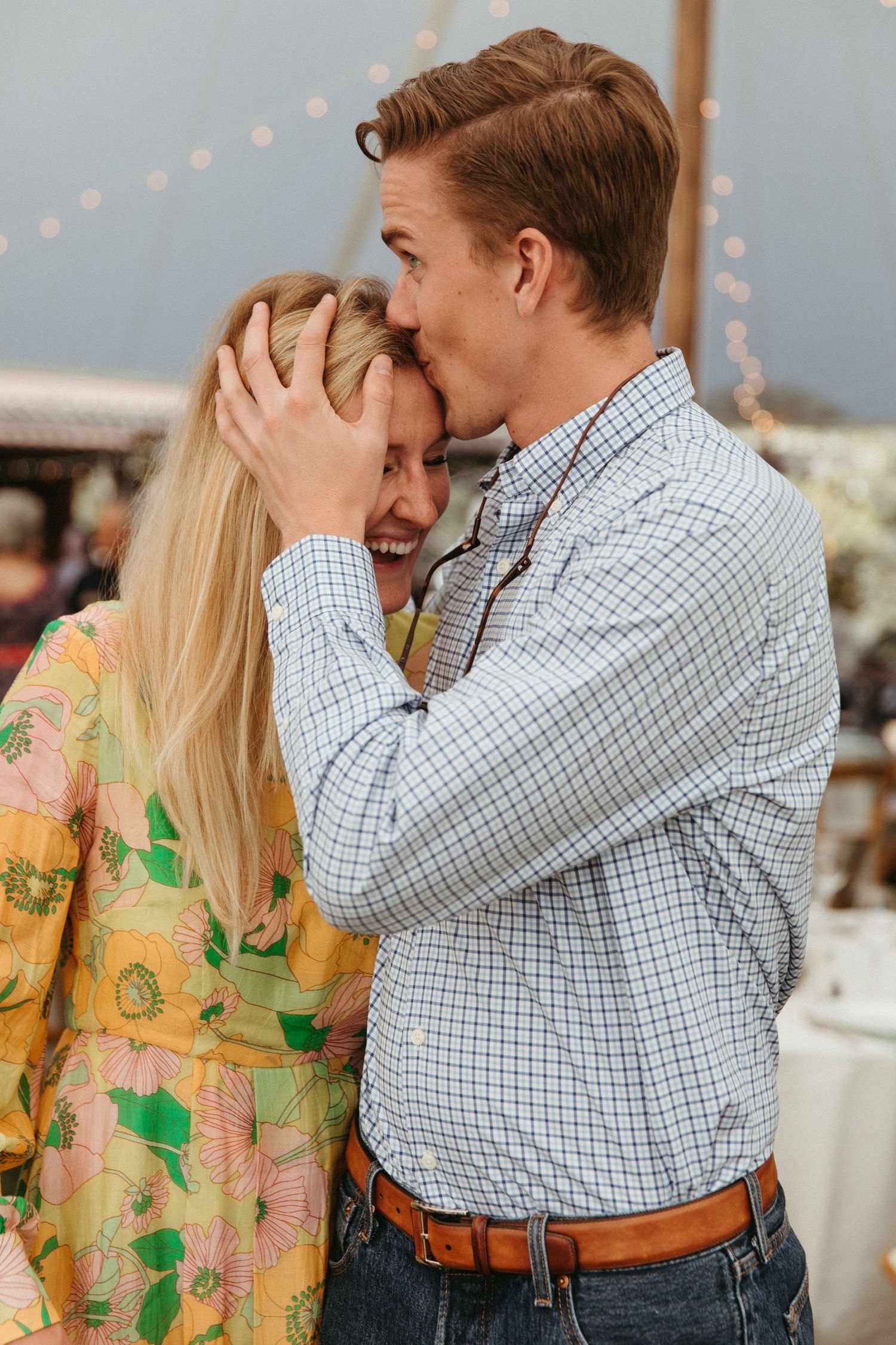 Couple sharing an intimate moment at an outdoor celebration with string lights in background.