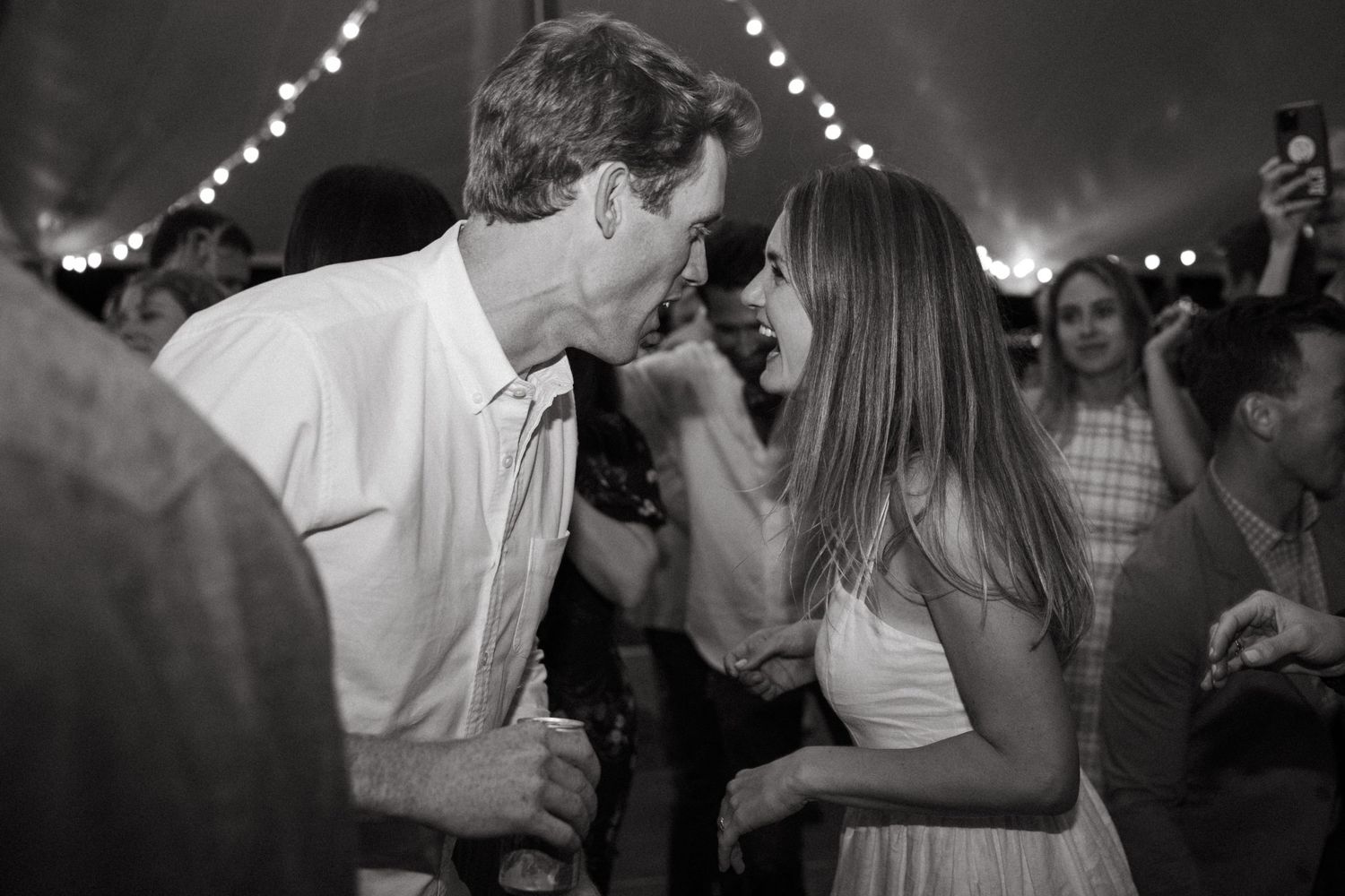 Black and white photo capturing an intimate dance moment under twinkling lights at a celebration.