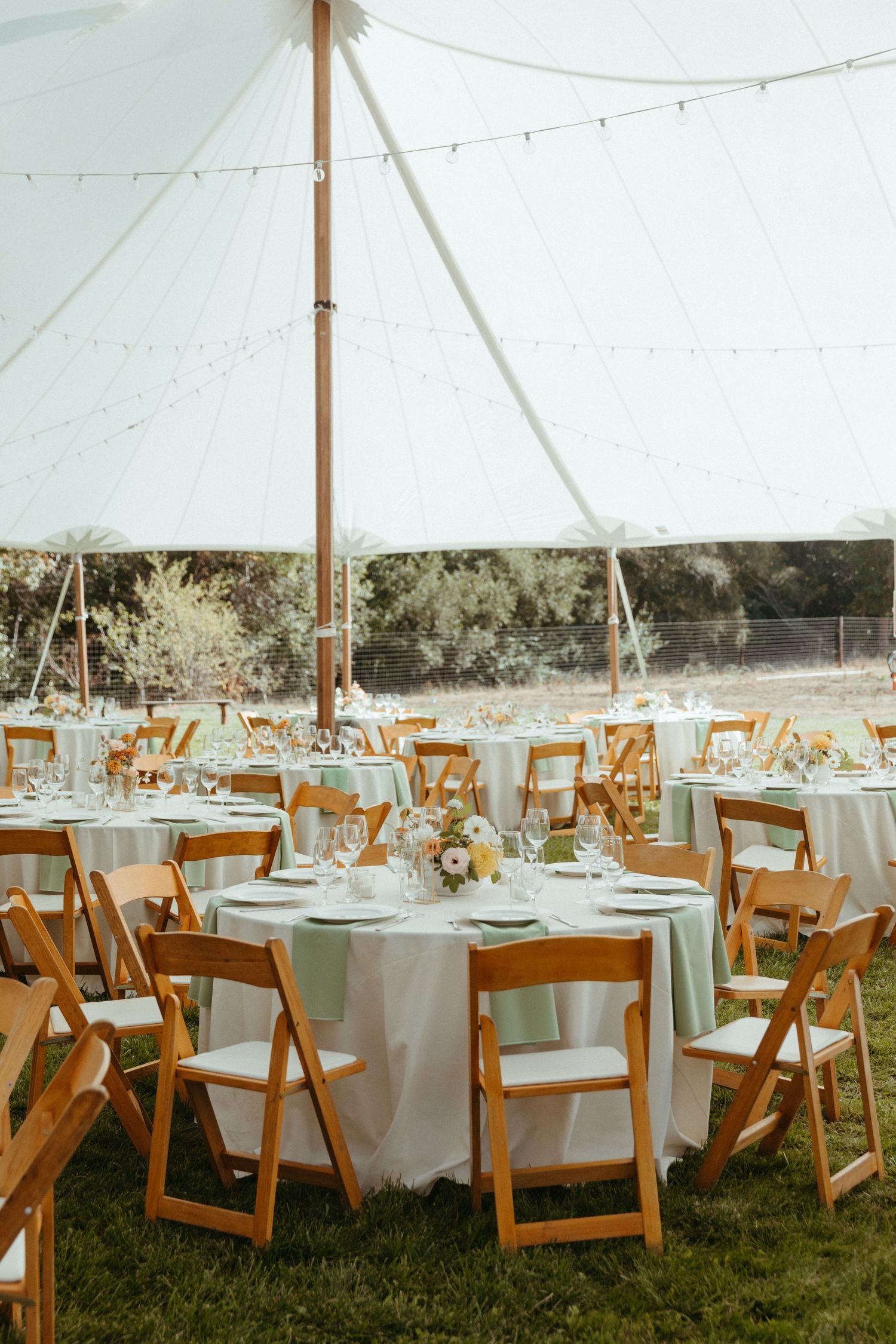 Elegant outdoor wedding reception setup with white tent and wooden folding chairs.