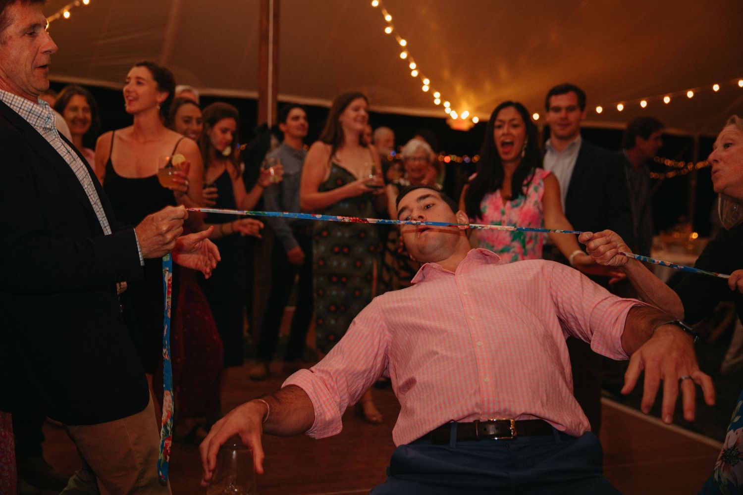 Person in pink shirt limboing under a bar at indoor celebration.