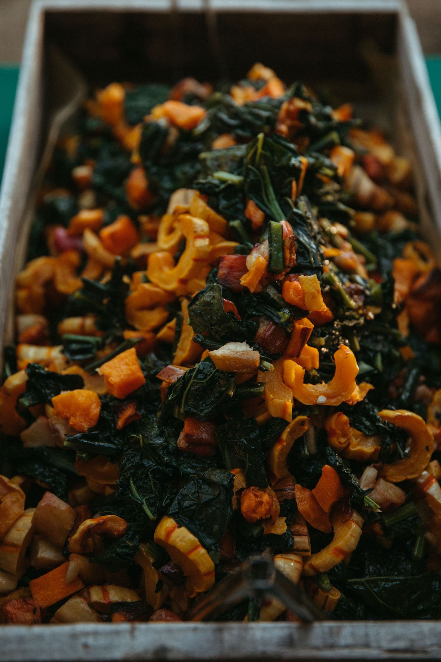 Rustic wooden tray filled with roasted butternut squash and dark leafy greens.