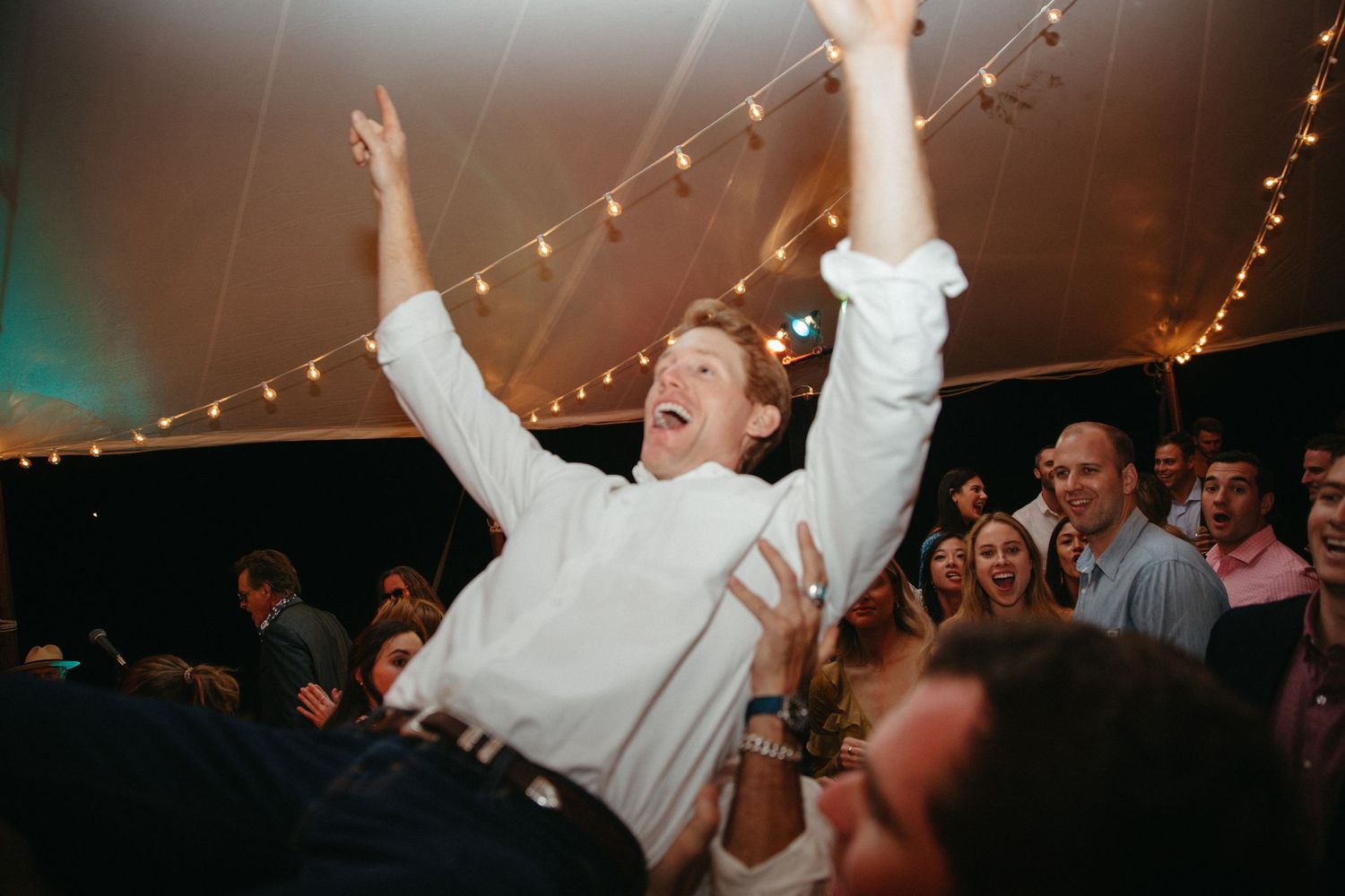 Person in white being lifted by a cheering crowd at a celebration.