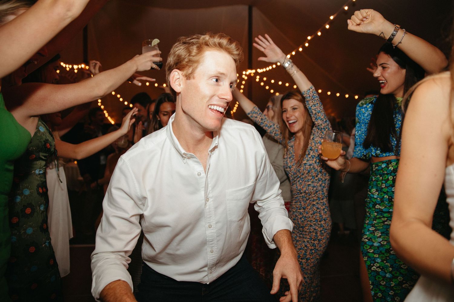 Dancing guests celebrate under string lights at wedding reception.