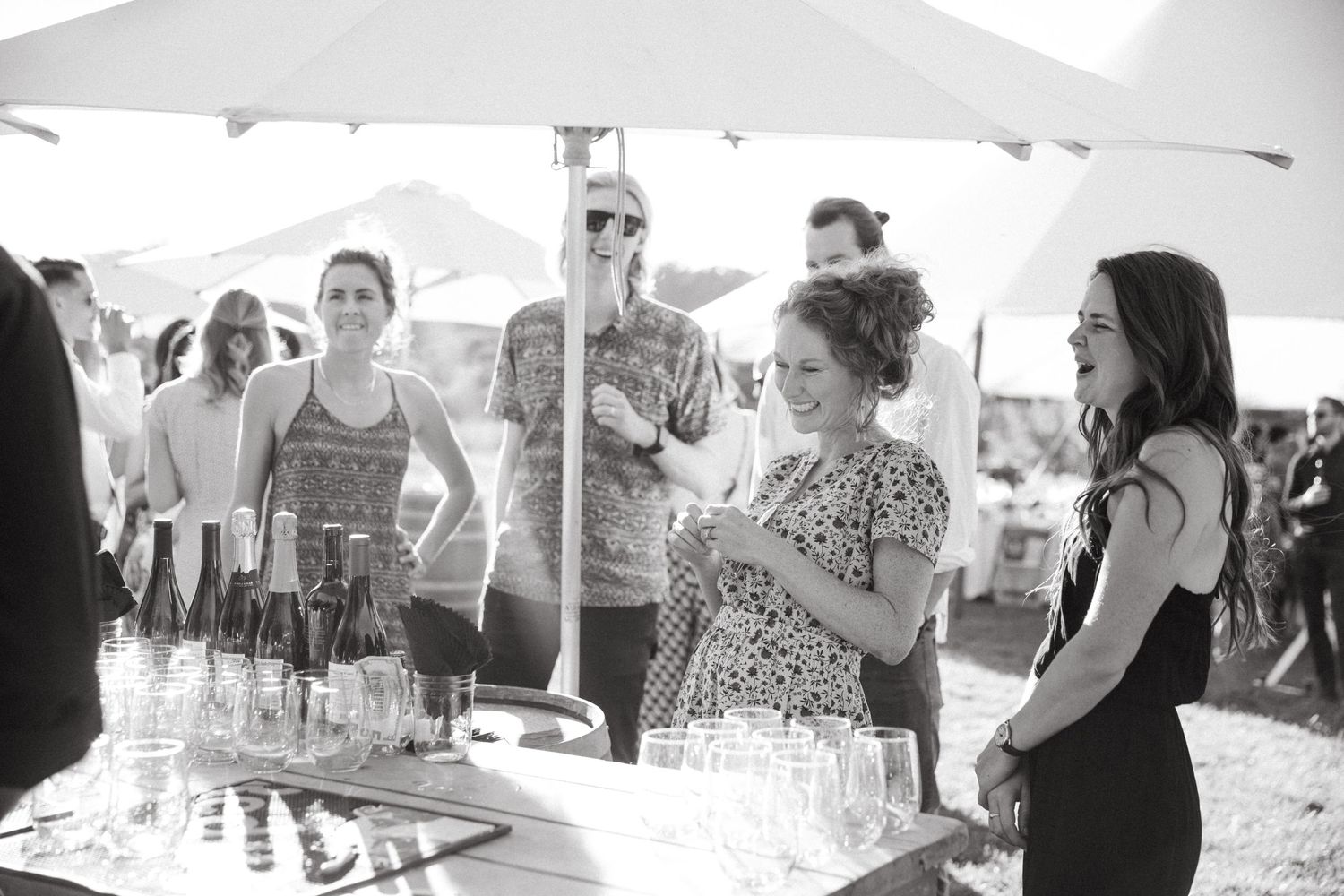 People gathered around a drink station under white umbrellas at an outdoor event.