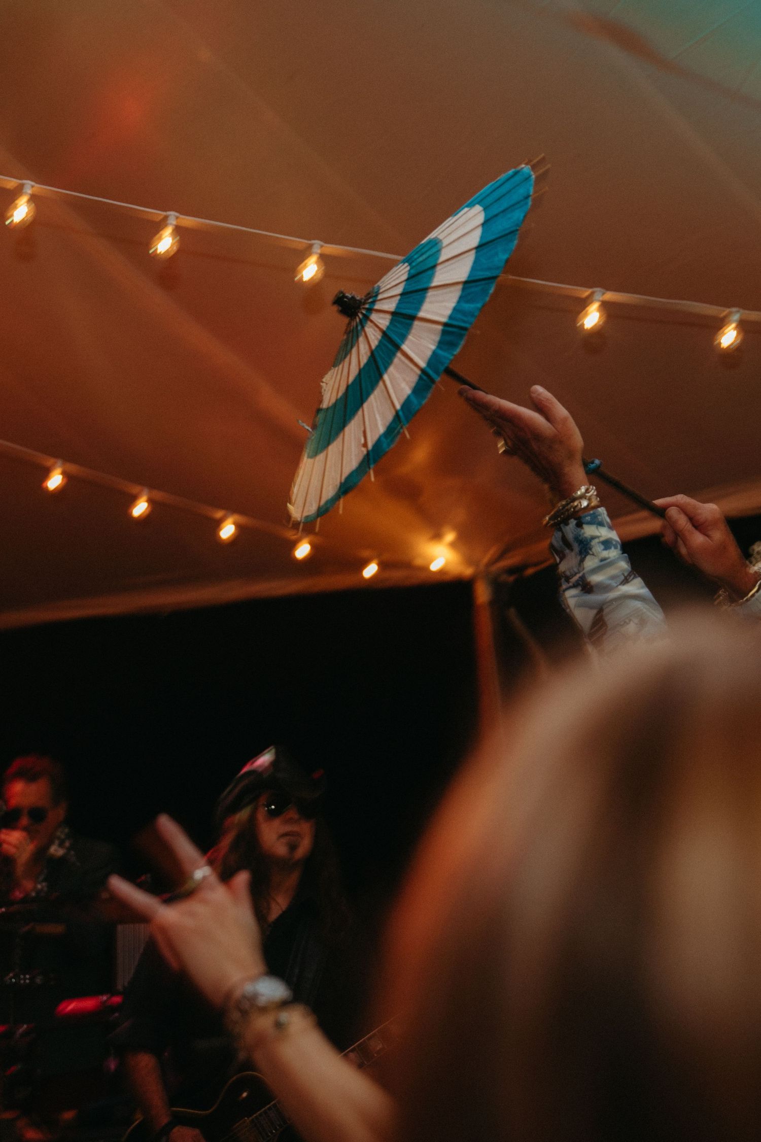 A blue paper parasol is held up against string lights at an evening celebration.