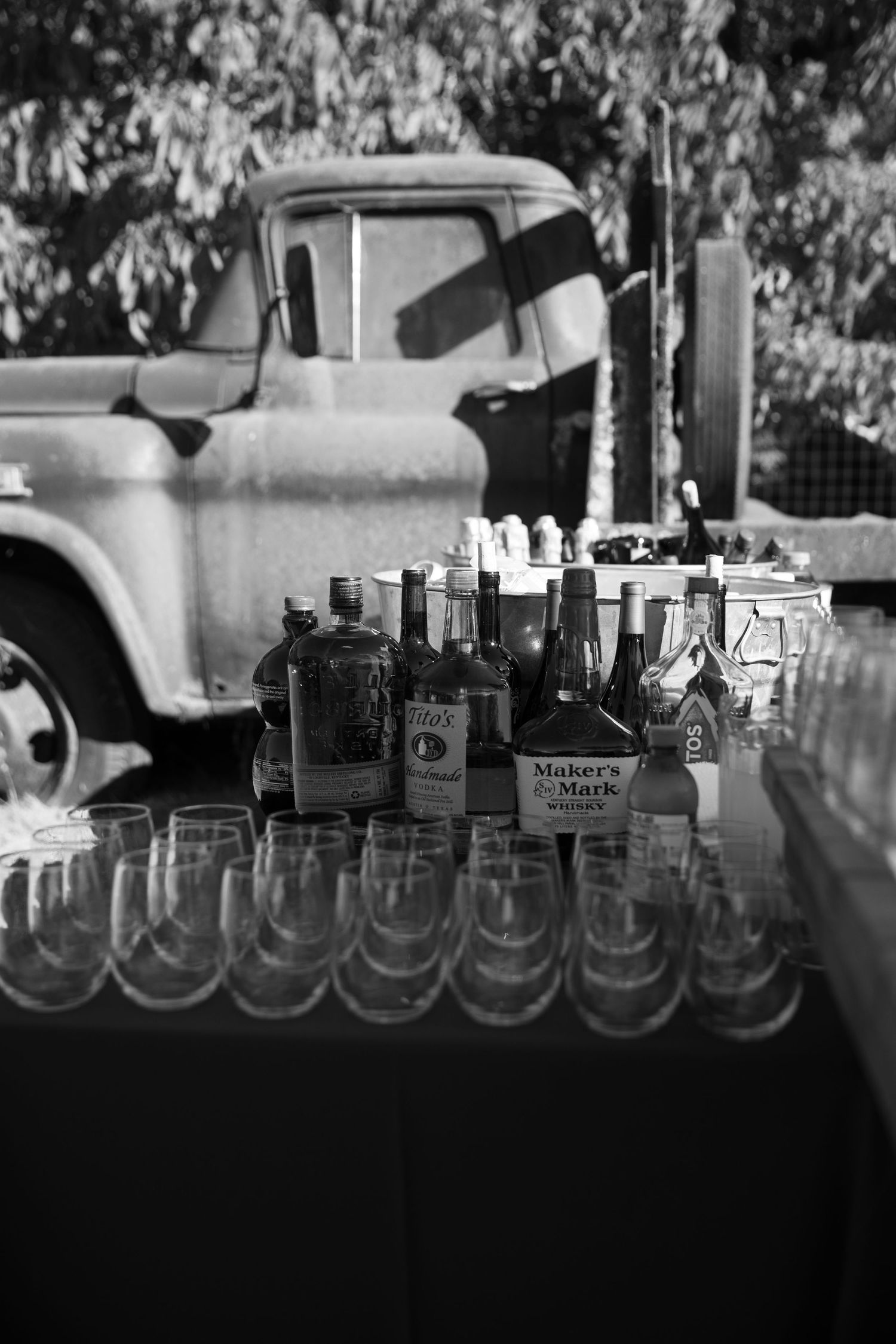 Vintage pickup truck with bottles and glasses arranged at a rustic bar setup in black and white.