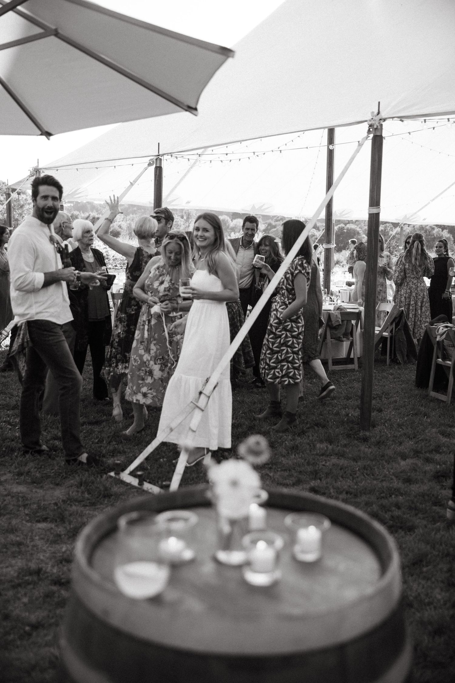 People celebrating at an outdoor party under a white tent with string lights.
