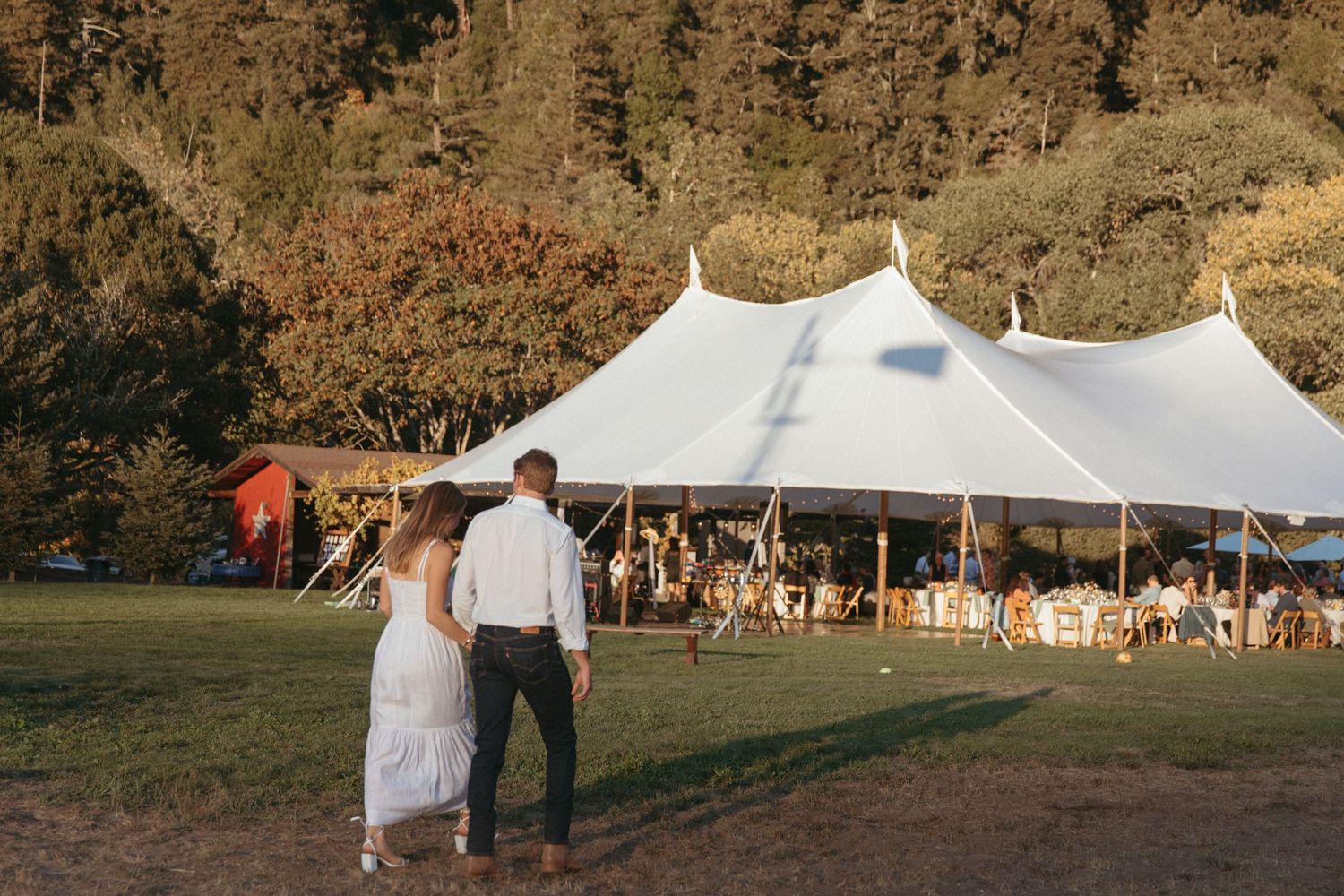 White wedding tent set up in field with mountain backdrop at sunset.