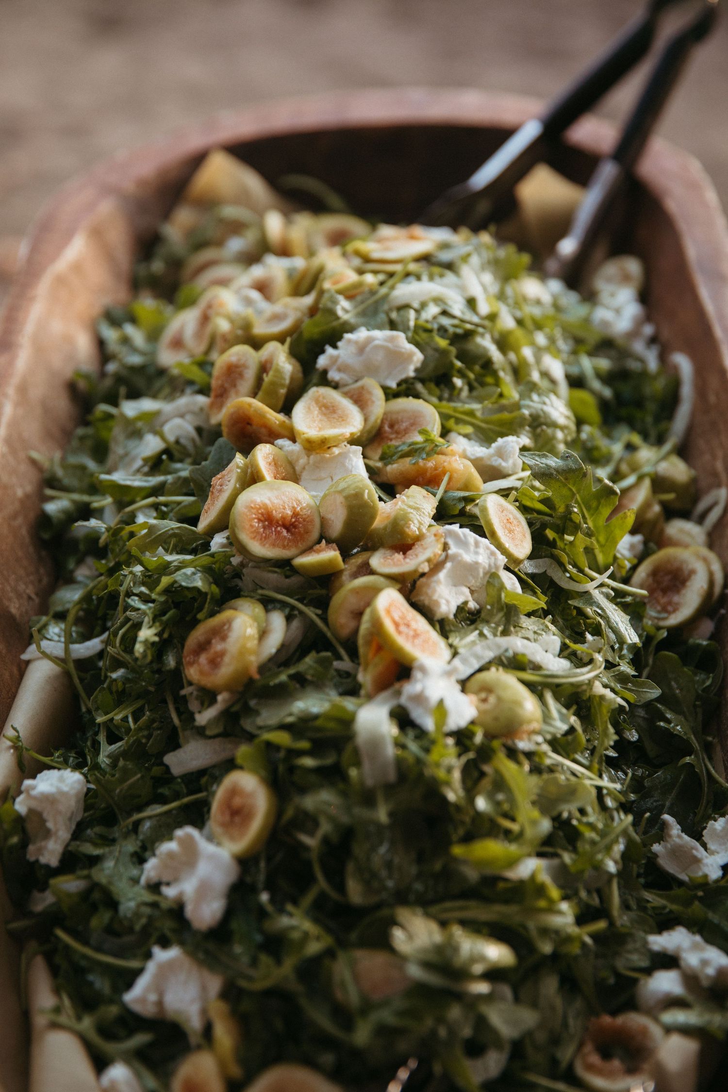 Fresh green salad topped with toasted hazelnuts and cheese in wooden serving bowl.