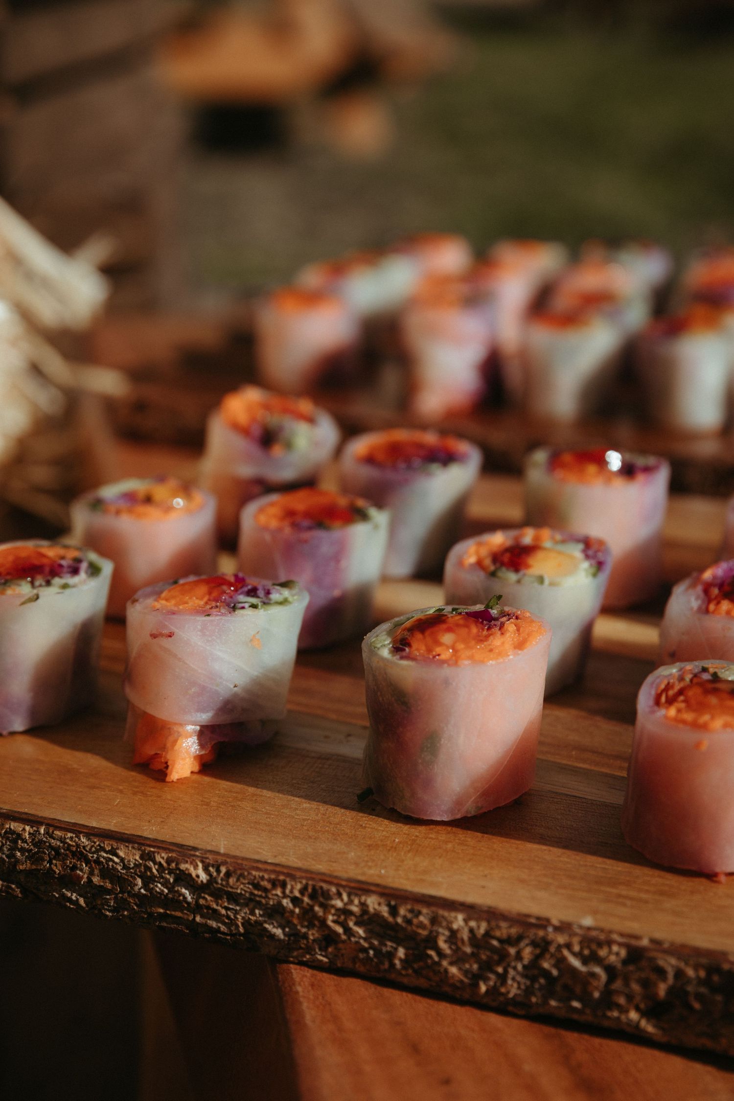 Artfully plated sushi rolls arranged on wooden serving board at catered event.