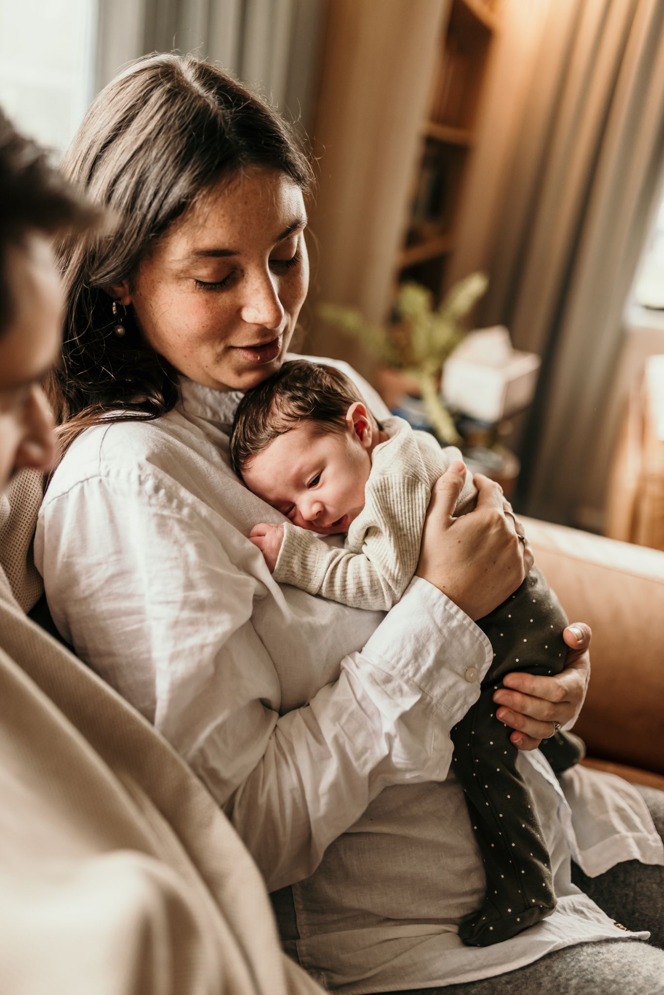 Tender moment between mother and sleeping baby in white clothing.