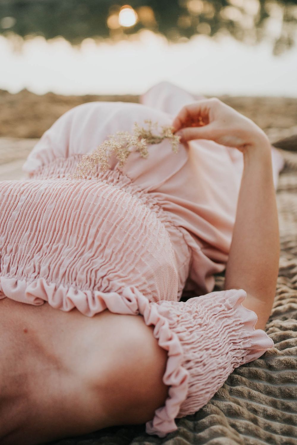 przyszła mama leży na plaży i gładzi swój ciążowy brzuszek - sesja ciążowa Kraków