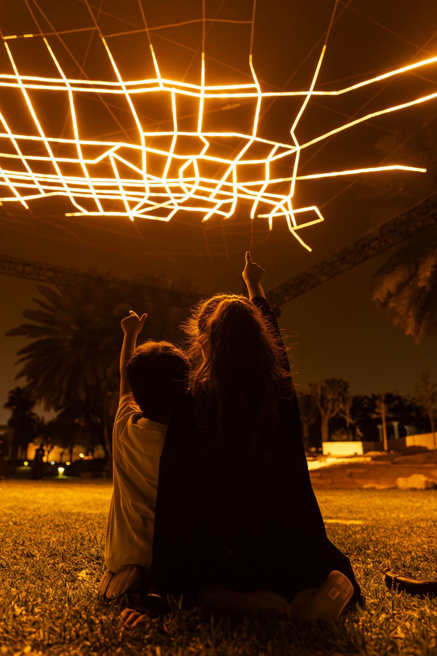 Silhouettes beneath glowing geometric light installation during nighttime.