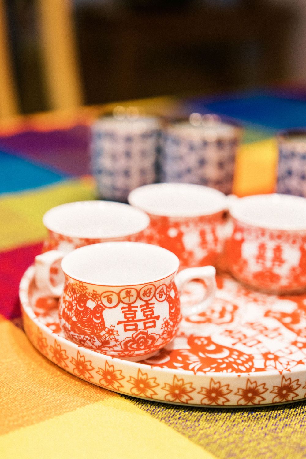 Traditional Chinese double happiness teacups in red and white on colorful tablecloth.