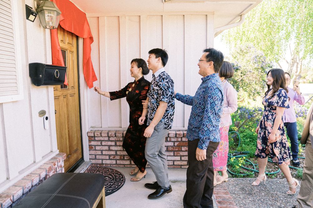Group stands at doorway during traditional Chinese wedding door games with red decorations.