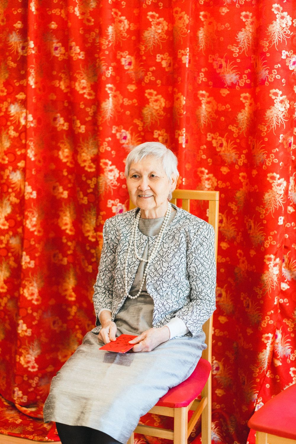 Person seated against vibrant red and gold patterned curtain backdrop.