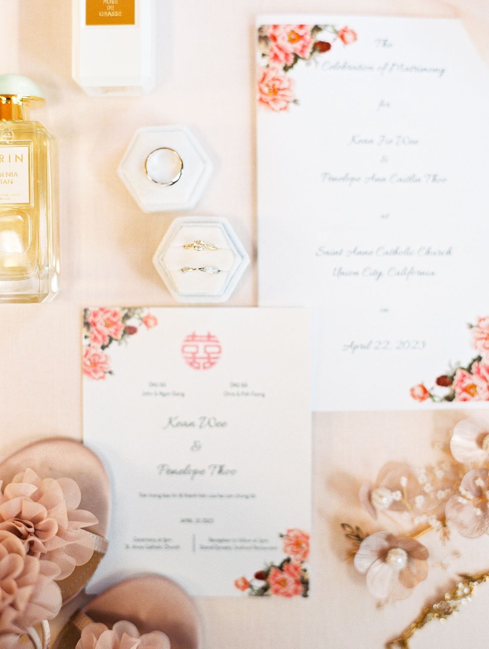 Wedding invitation suite with floral design, perfume bottle and ring display on pink surface.