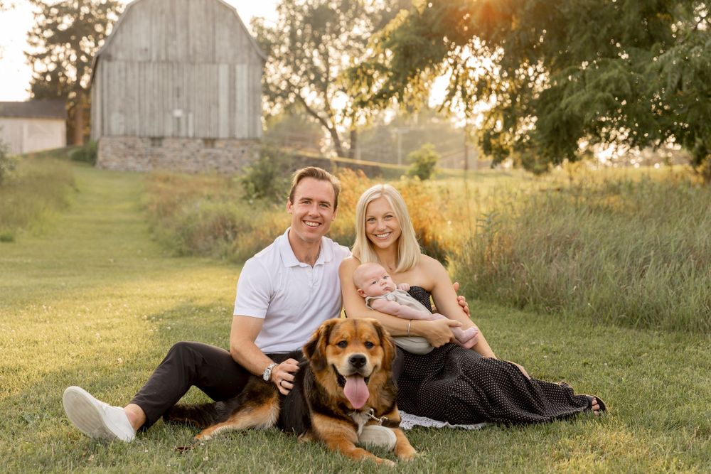 family with a newborn and a dog sits to pose for a photo in front of a barn in troy Michigan
