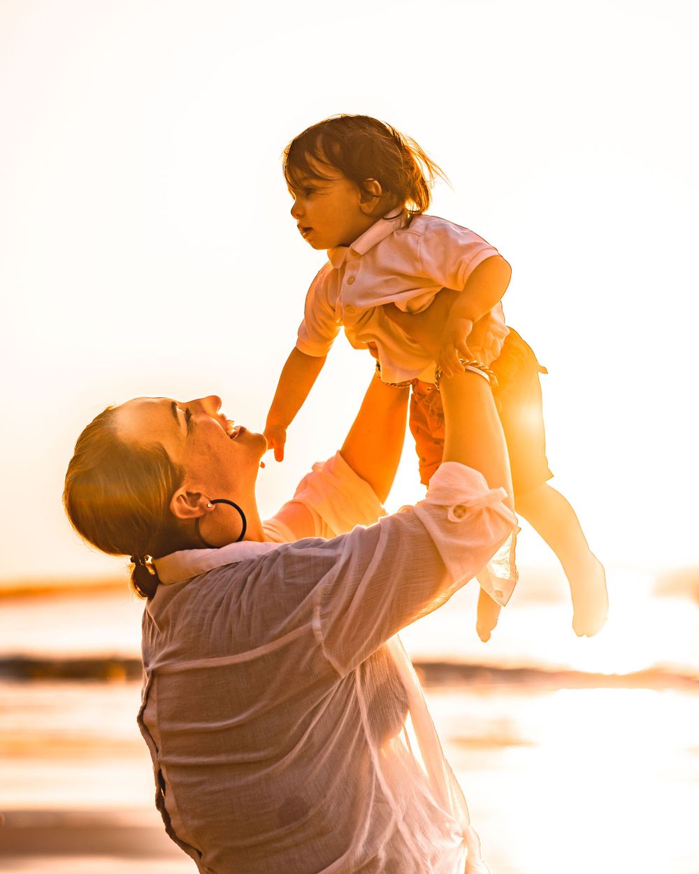 A Mother holding her son up in the air on the beach at sunset