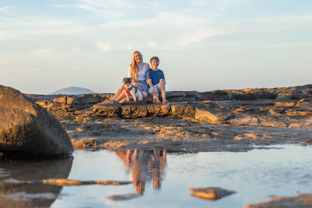 Photo of a mother and her son sitting on a rock at point Cartwright Sunshine Coast during sunset with their reflection in the water