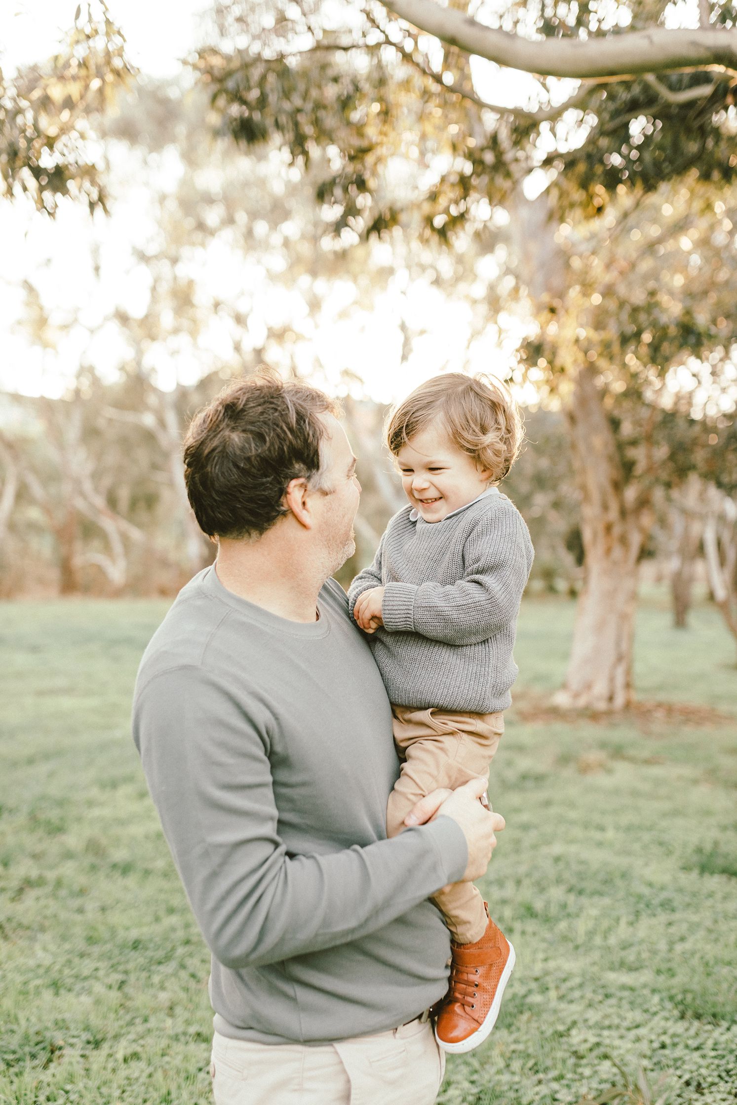 Heartwarming interaction between parent and child both wearing grey sweaters in a park setting.