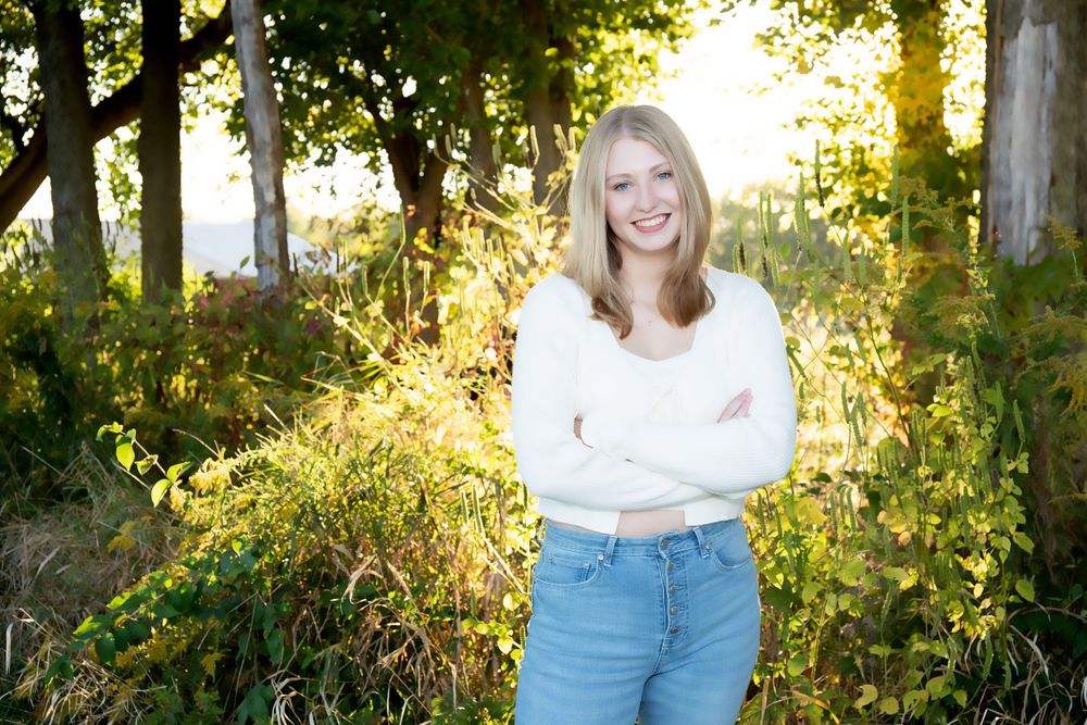 Outdoor portrait against backlit trees with warm golden sunlight filtering through leaves.