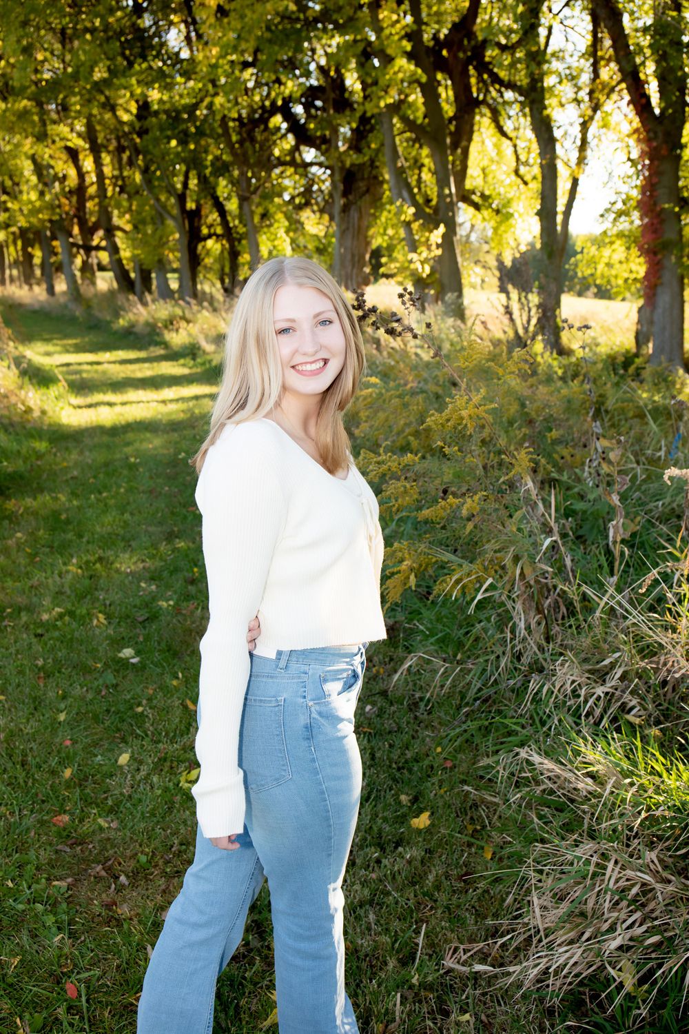 Candid outdoor portrait with autumn trees wearing white sweater and light wash denim.