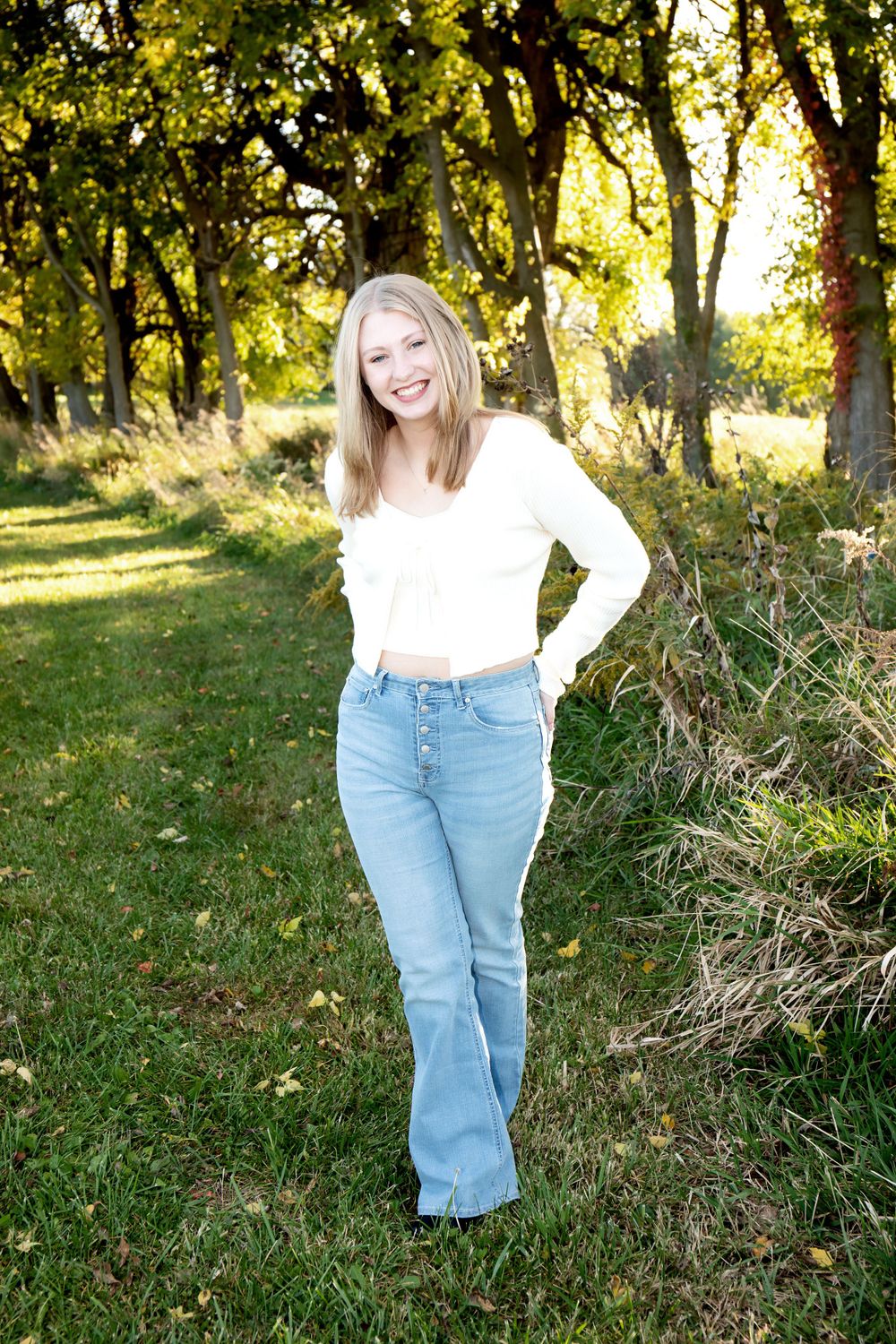 Cheerful outdoor portrait in white top and jeans with golden autumn trees in background.