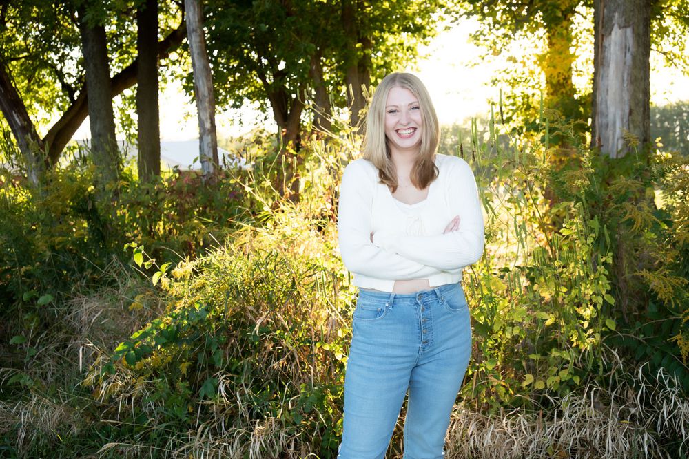 Backlit autumn scene with person in white sweater and jeans standing among trees.