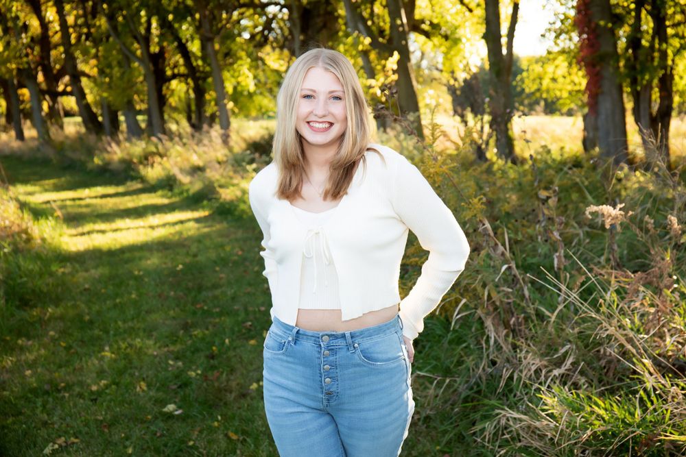 Sunny outdoor portrait against golden trees wearing white sweater and blue jeans.