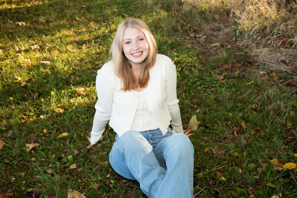 Casual outdoor portrait in autumn setting with trees and fallen leaves.
