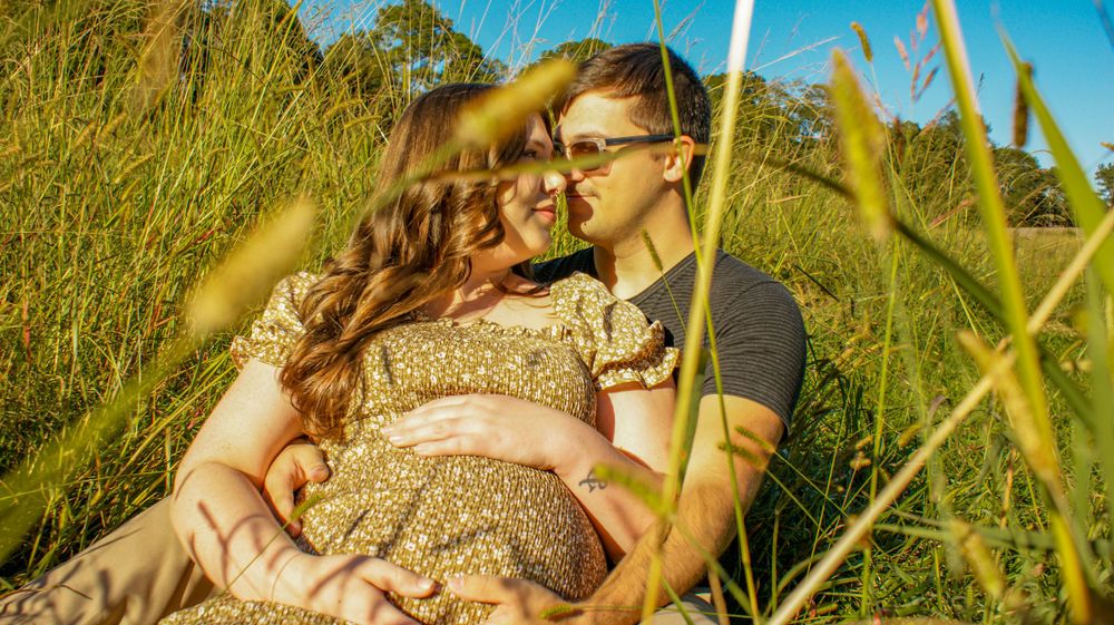 Romantic maternity photo session in a sunlit field with tall grass.
