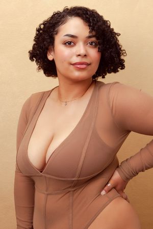Lifestyle portrait session in a beige form-fitting top against a warm toned wall.