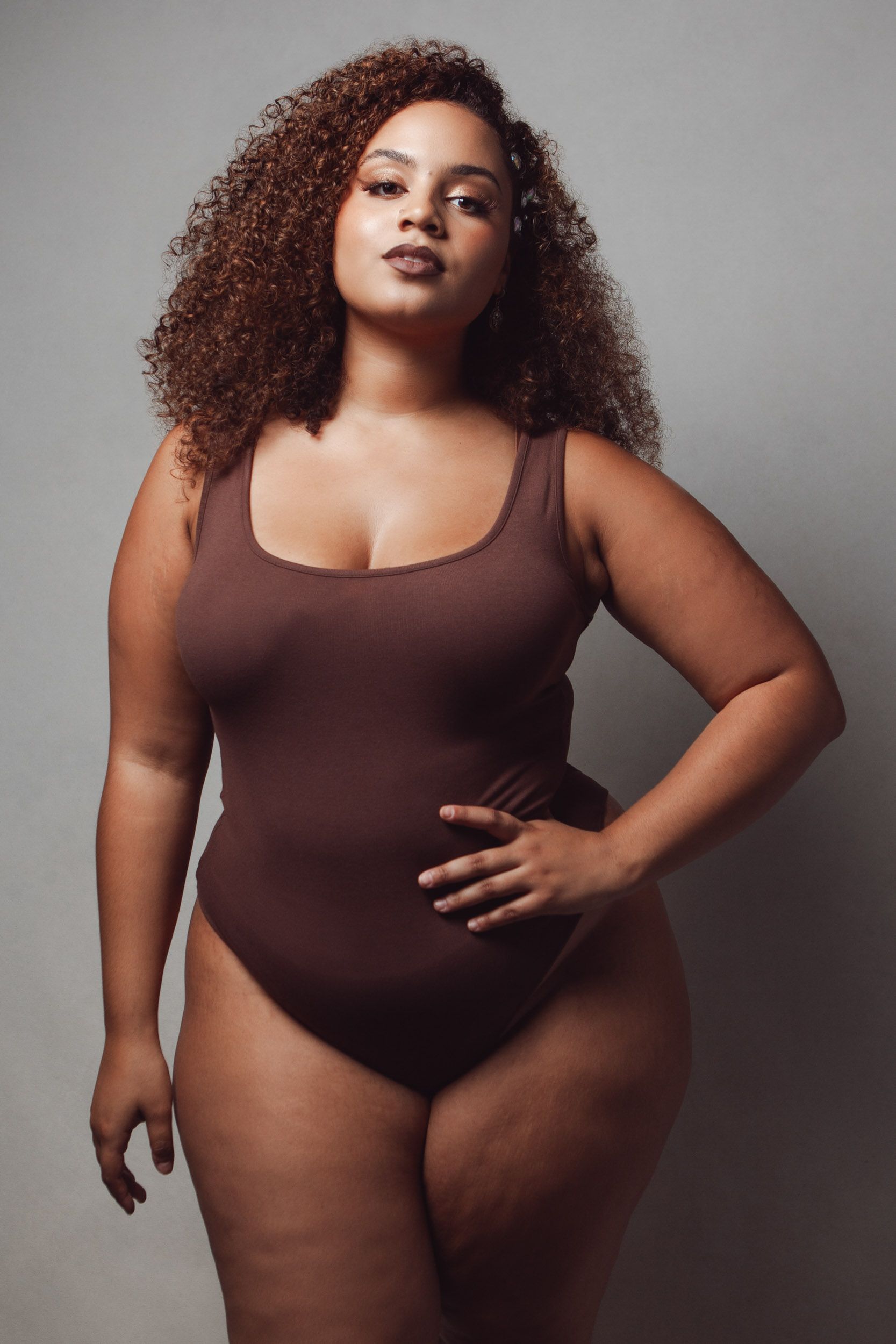 Body positive portraits in brown bodysuit showing natural curves and confidence.