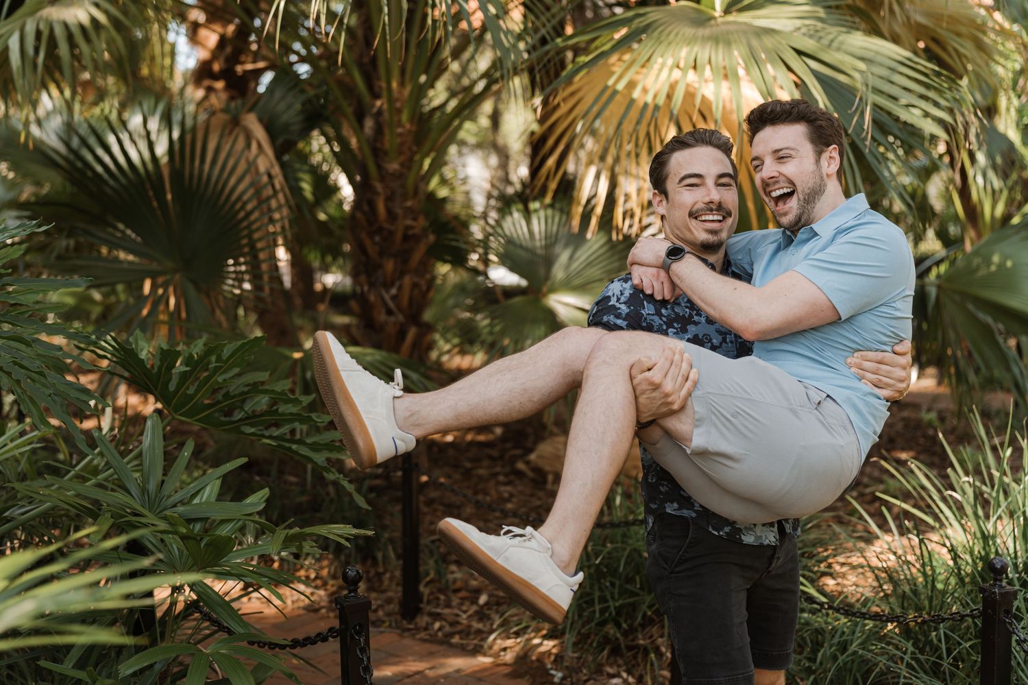 A playful outdoor photoshoot in a tropical garden setting with one person carrying another.