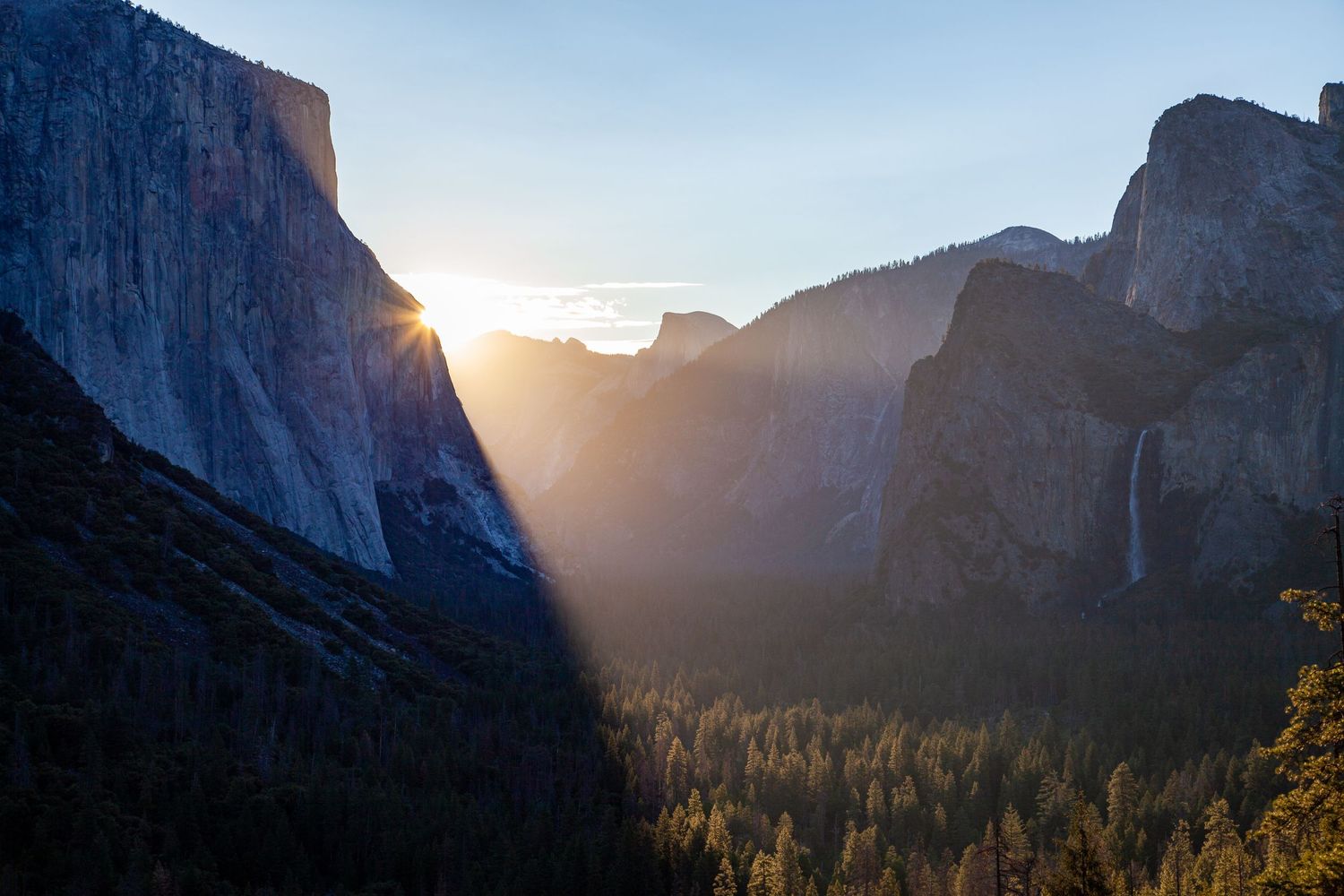 Golden sunlight streams through Yosemite Valley, illuminating towering granite cliffs and forested valley below.