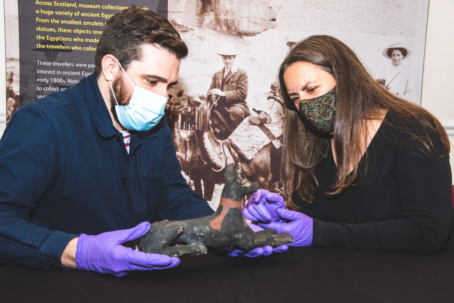Museum staff wearing masks and gloves inspect artifacts at an exhibition.