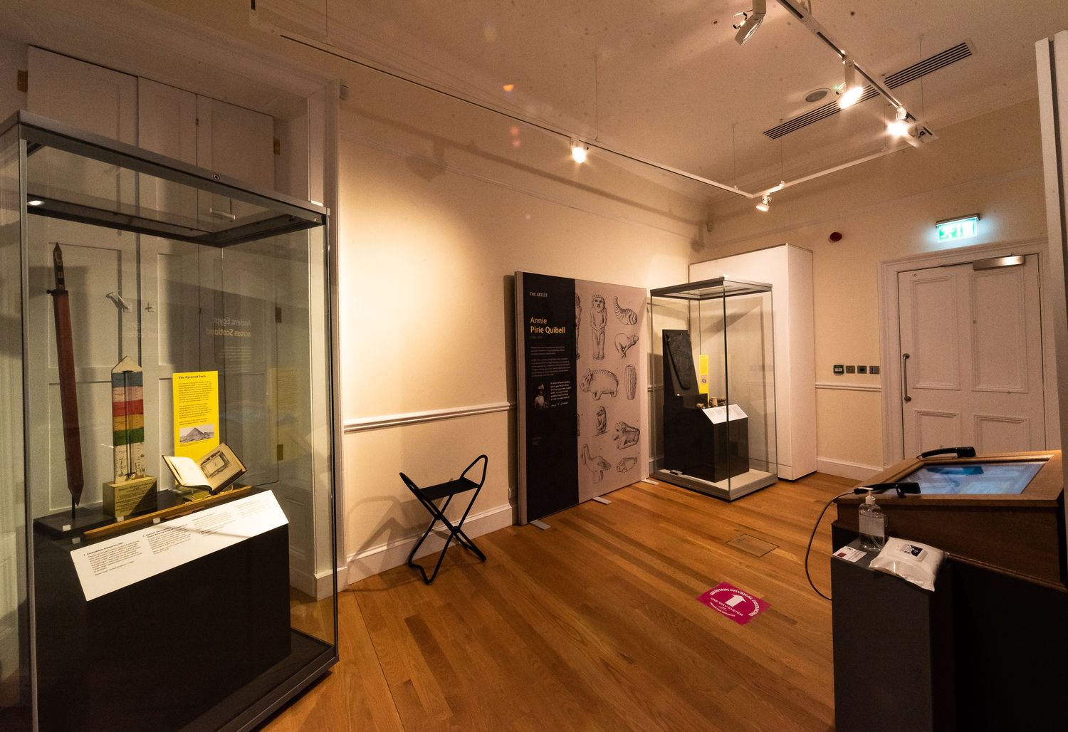 Museum exhibition area with glass cases and graphic panels illuminated by track lighting.