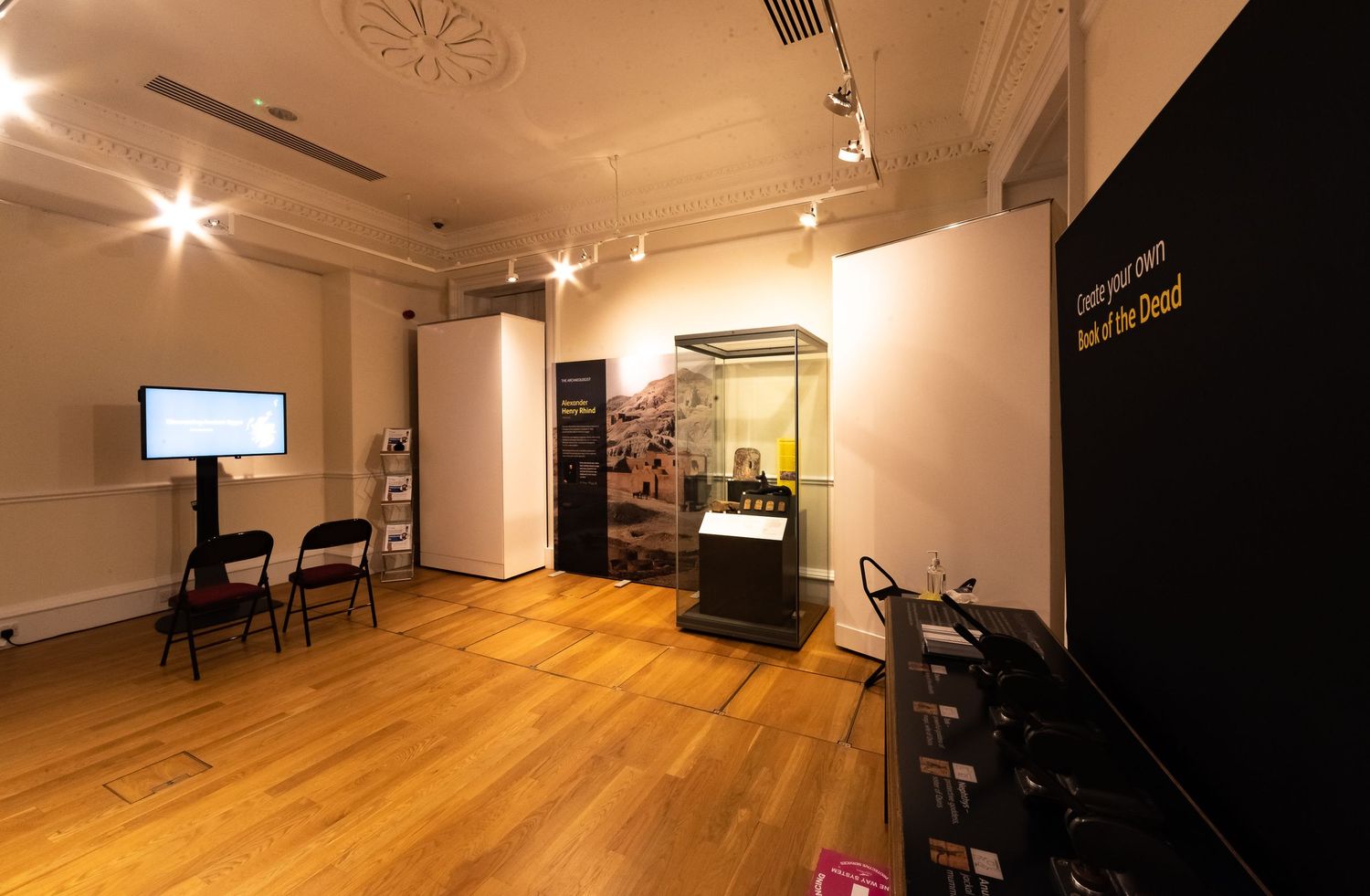 Interior view of a museum exhibition space with hardwood floors, display cases, and track lighting.