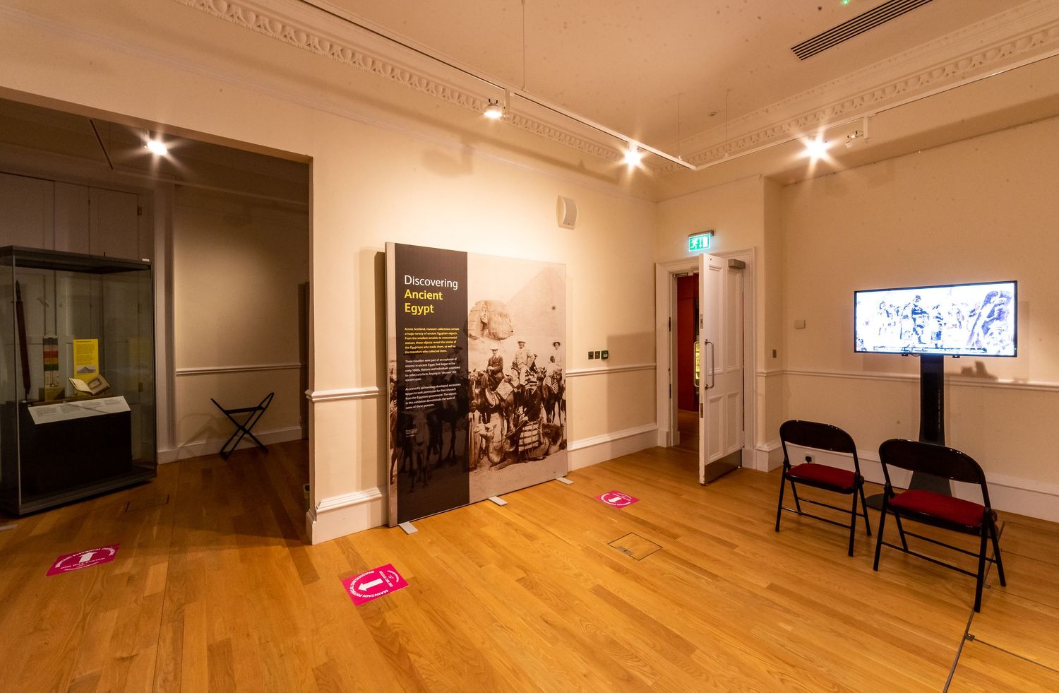Exhibition space featuring display cases and digital screens with ornate ceiling moldings.