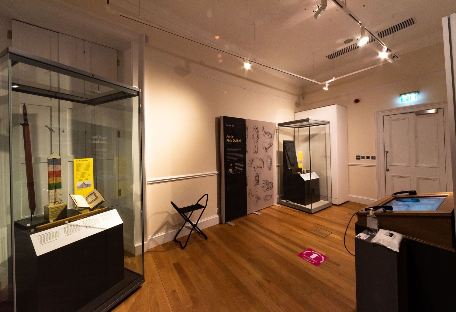 Gallery space featuring glass display cases and informational panels with wooden flooring.
